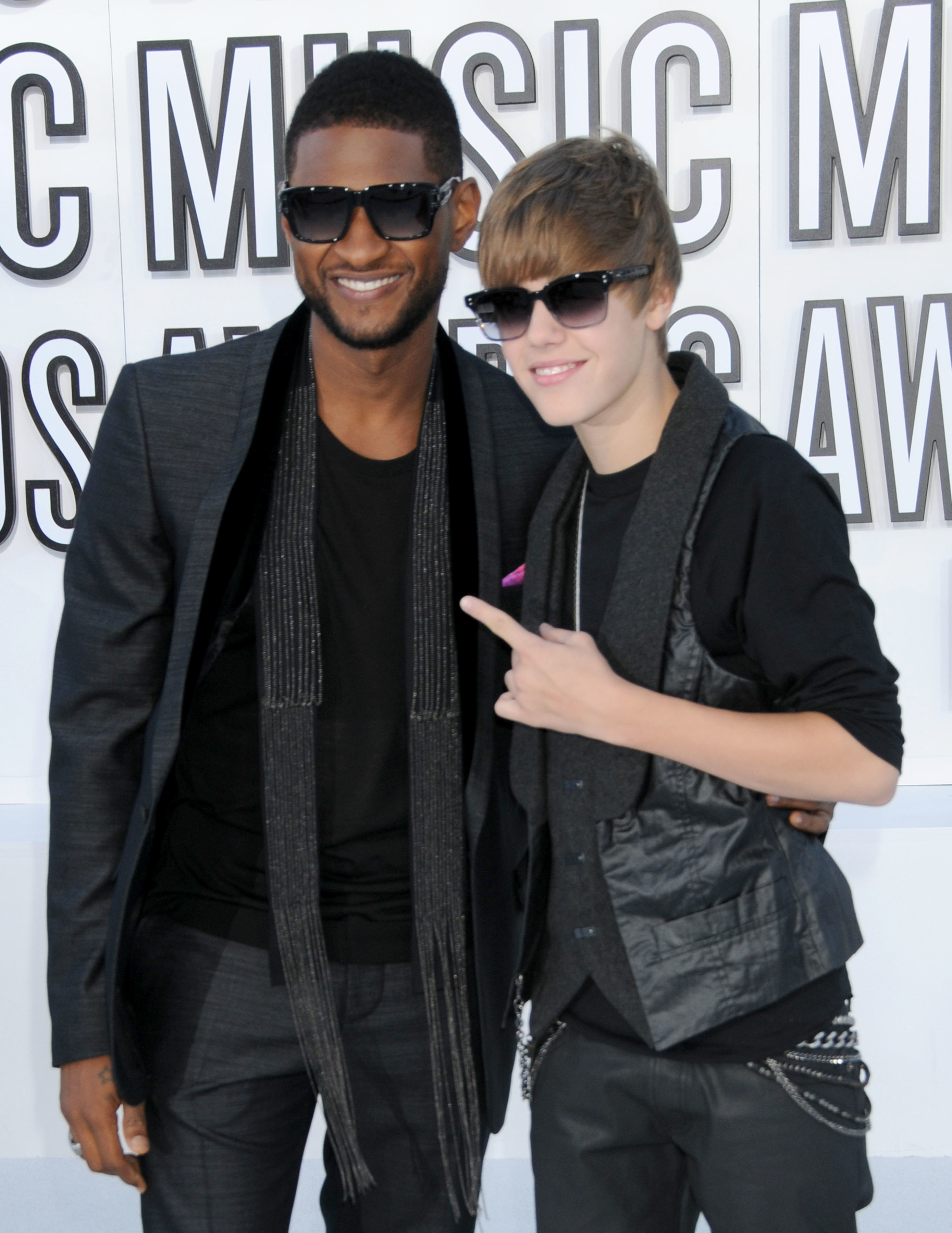 Usher in a black suit with a scarf and Justin Bieber in a black outfit with a vest posing at an awards event