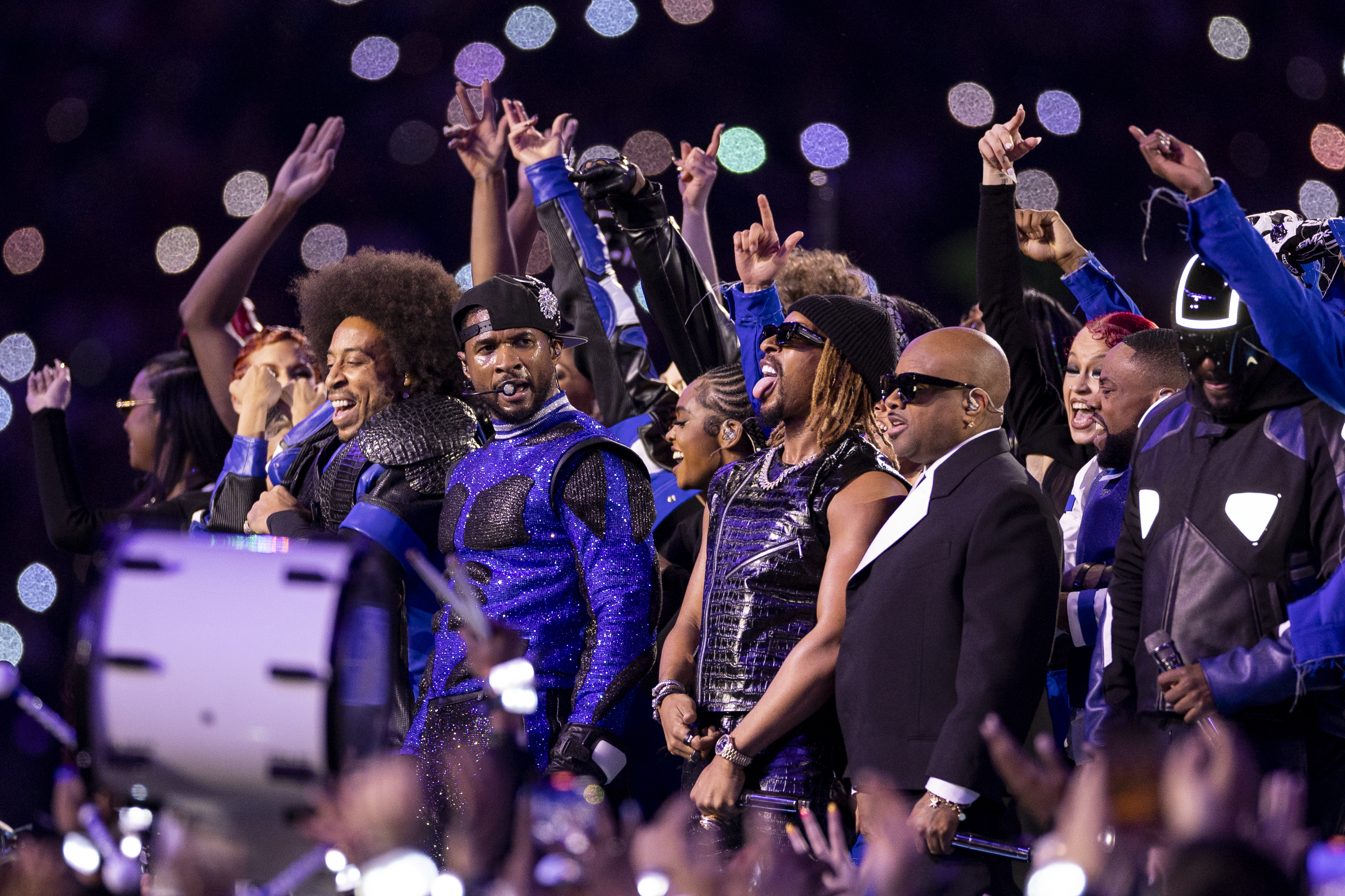 Usher and group of performers on stage with one in a sparkling blue outfit, celebrating under confetti