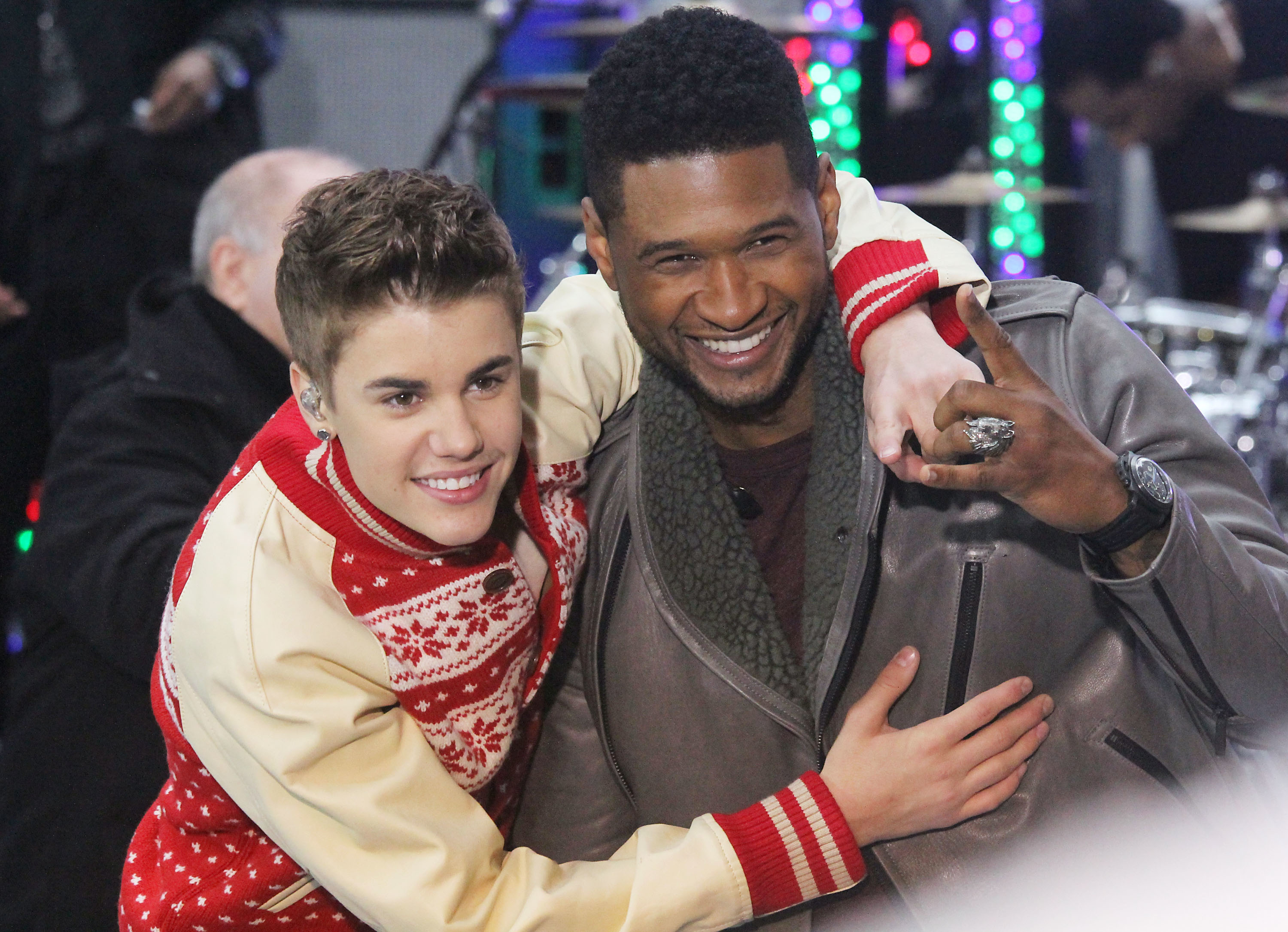 Justin Bieber and Usher smiling at a festive event, both in winter-themed attire