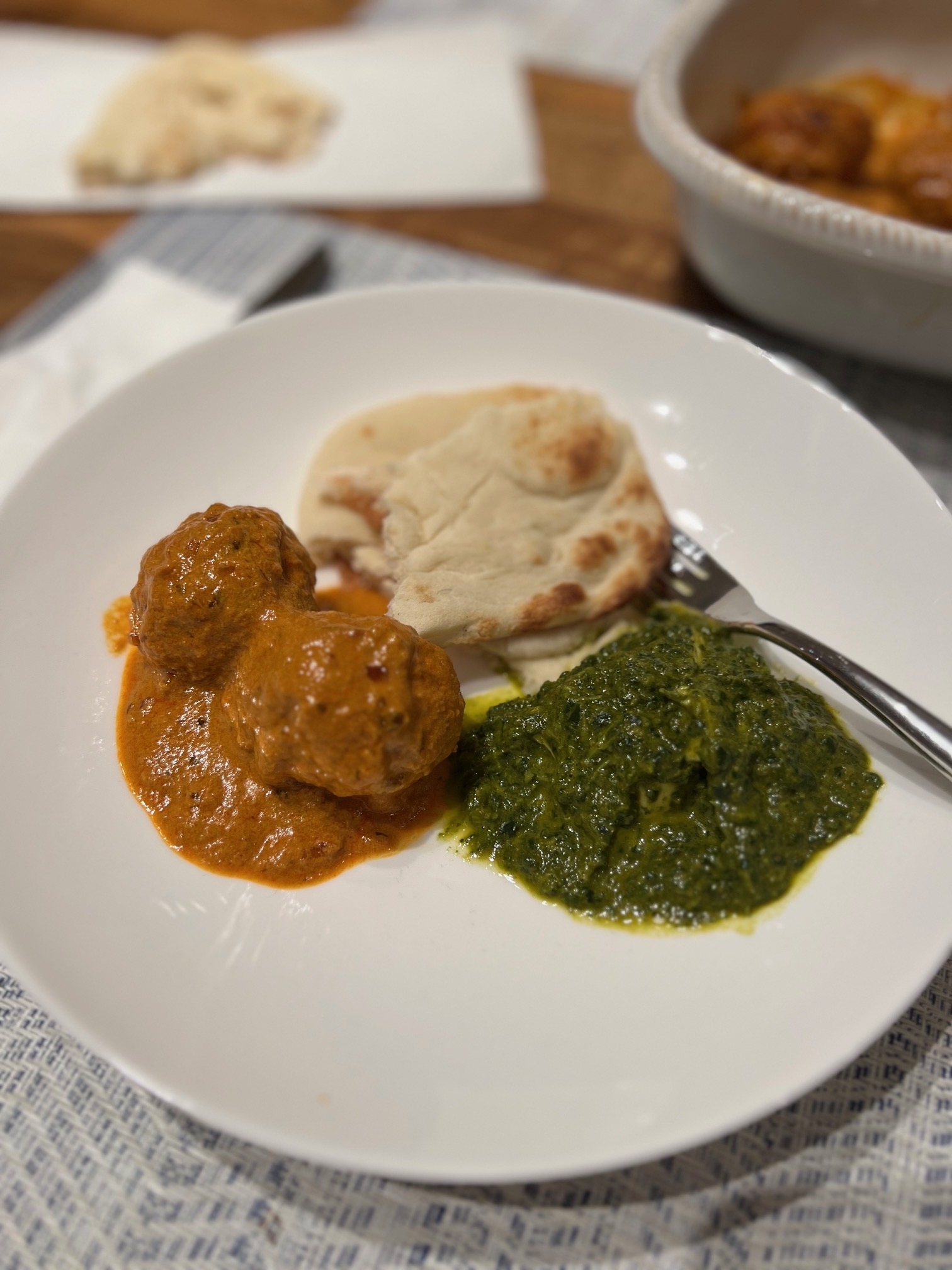Plate with meatballs in sauce, naan bread, and saag on a table