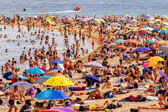 Crowded beach scene with people swimming and lounging under umbrellas