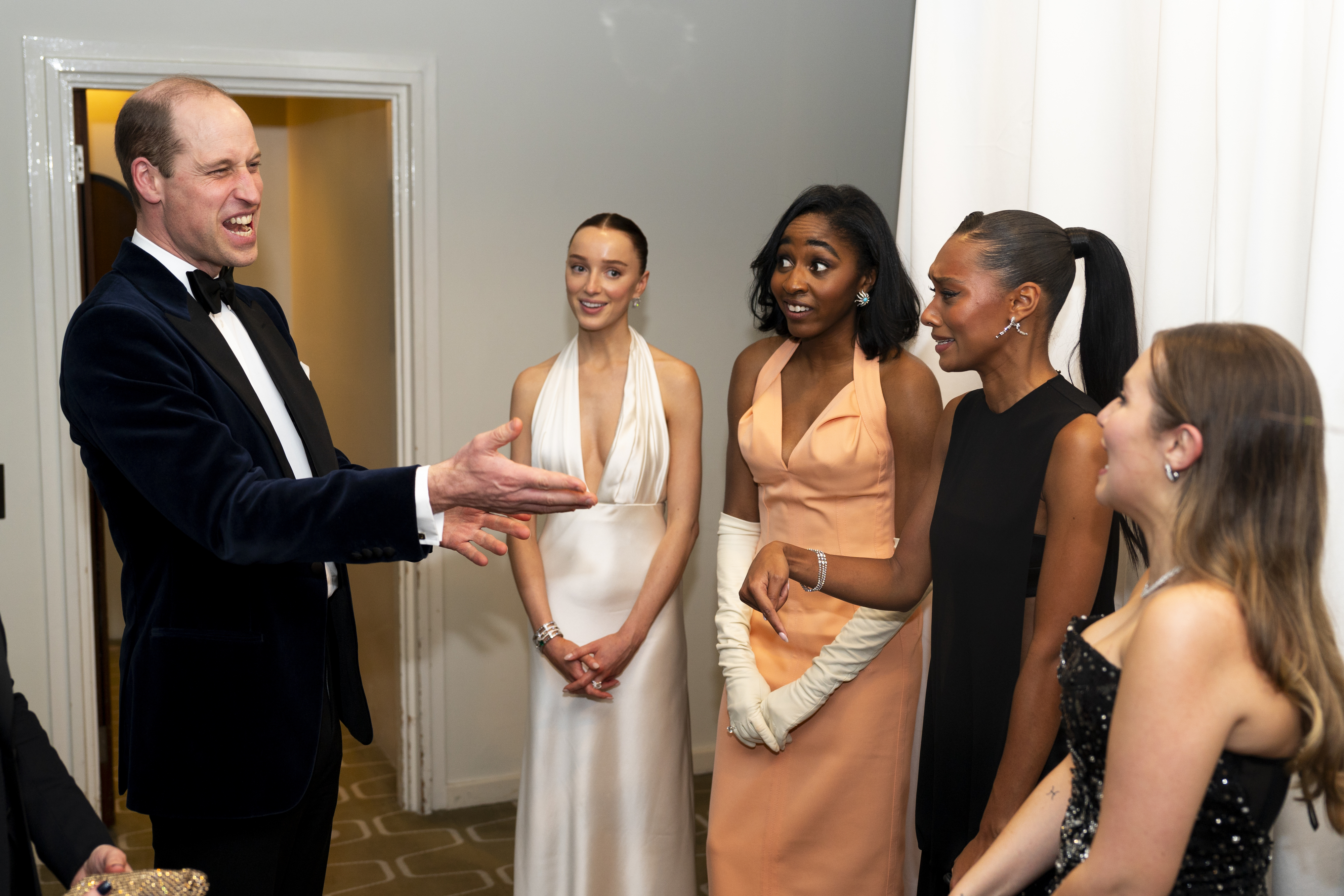 Four women in elegant evening wear interact with a man in a tuxedo at a formal event