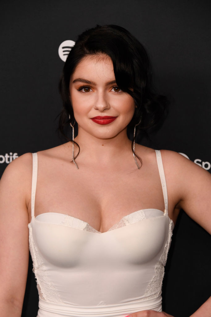 Ariel Winter posing in a dress with lace details, with her hair styled in waves, at an event