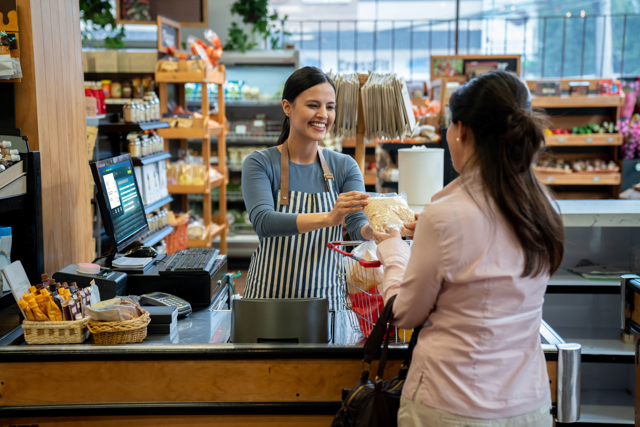Supermarket cashier smiling as she hands a bag of groceries to a customer at the checkout