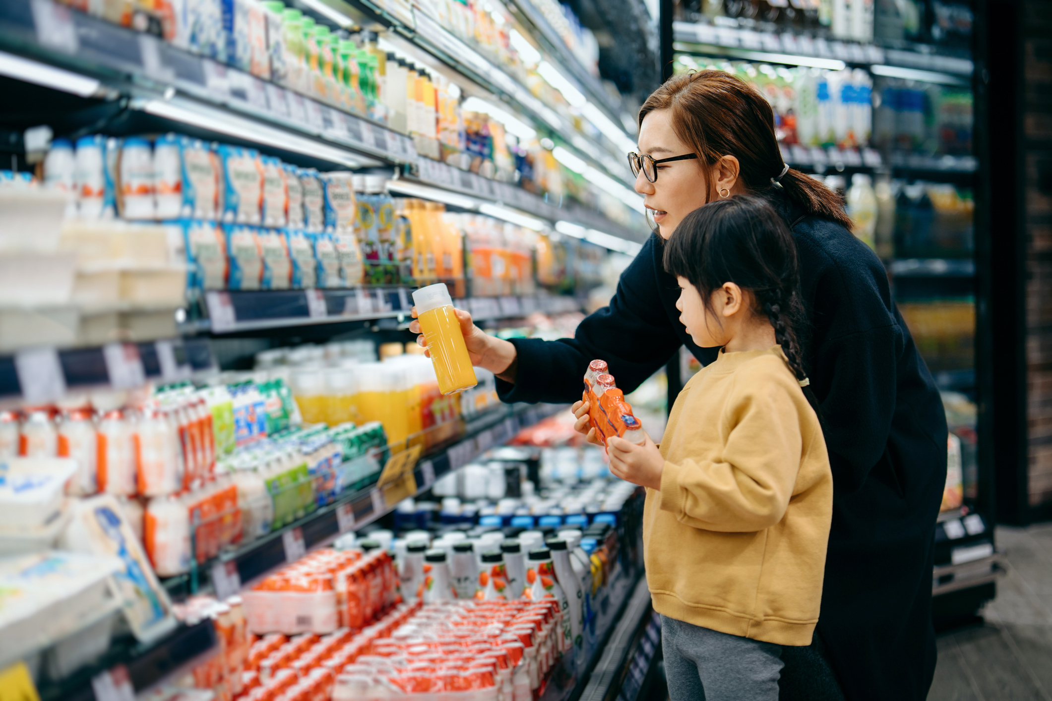 Adult and child selecting beverages from grocery store refrigerator section