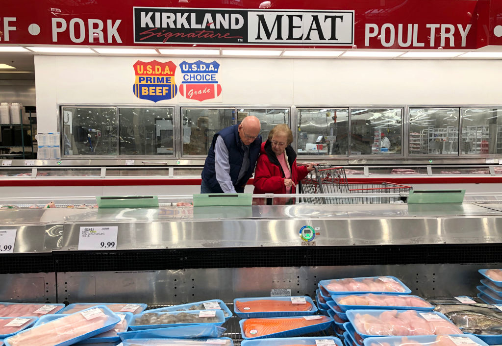 Two people shopping for meat at a Costco, standing behind a counter with various meat products