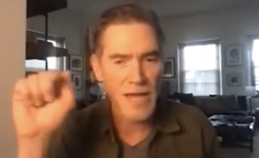 Billy speaking during a video call with a blurred interior background