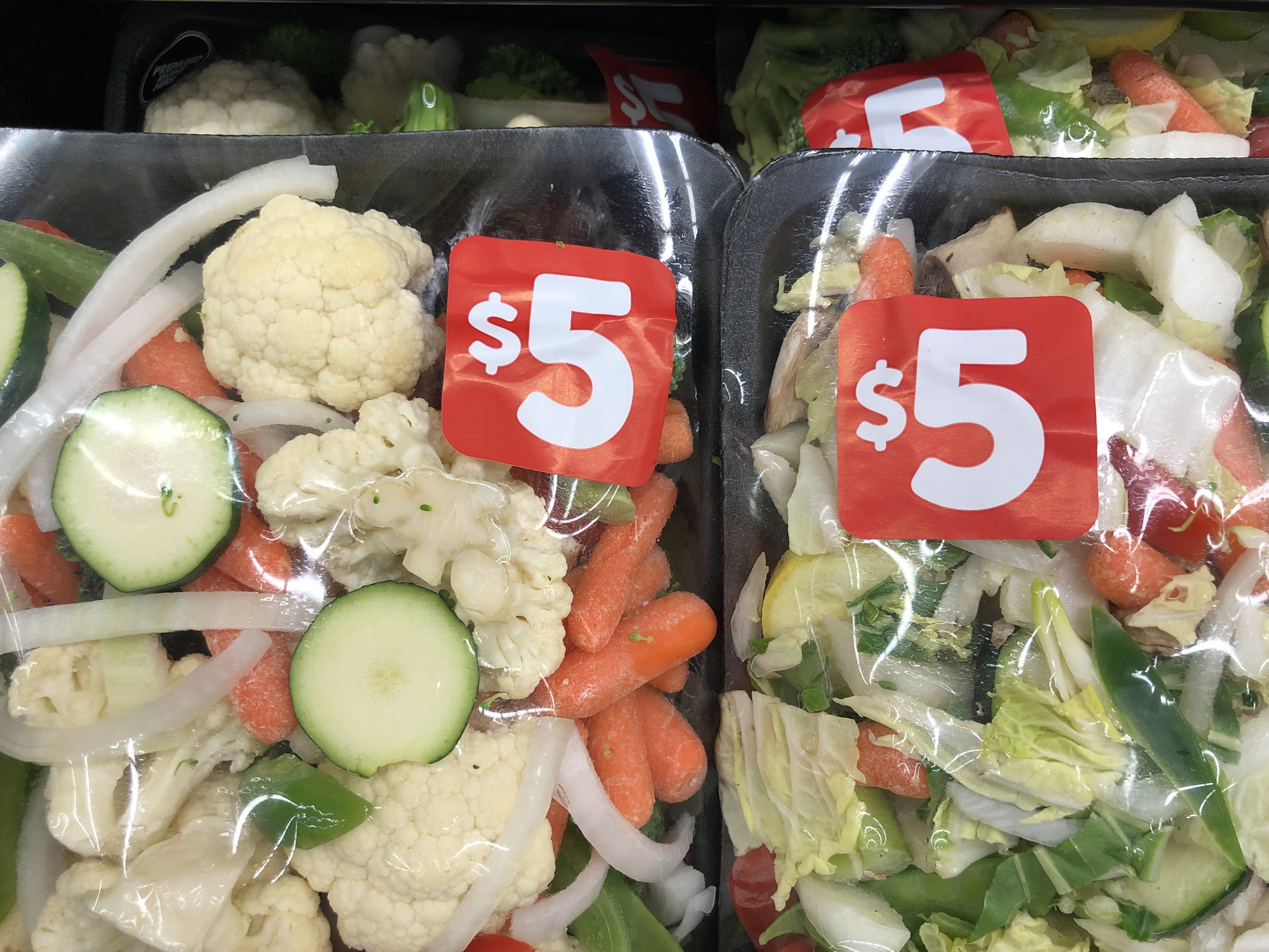 Pre-packaged vegetables for stir-fry, priced at $5 each, displayed in a grocery store