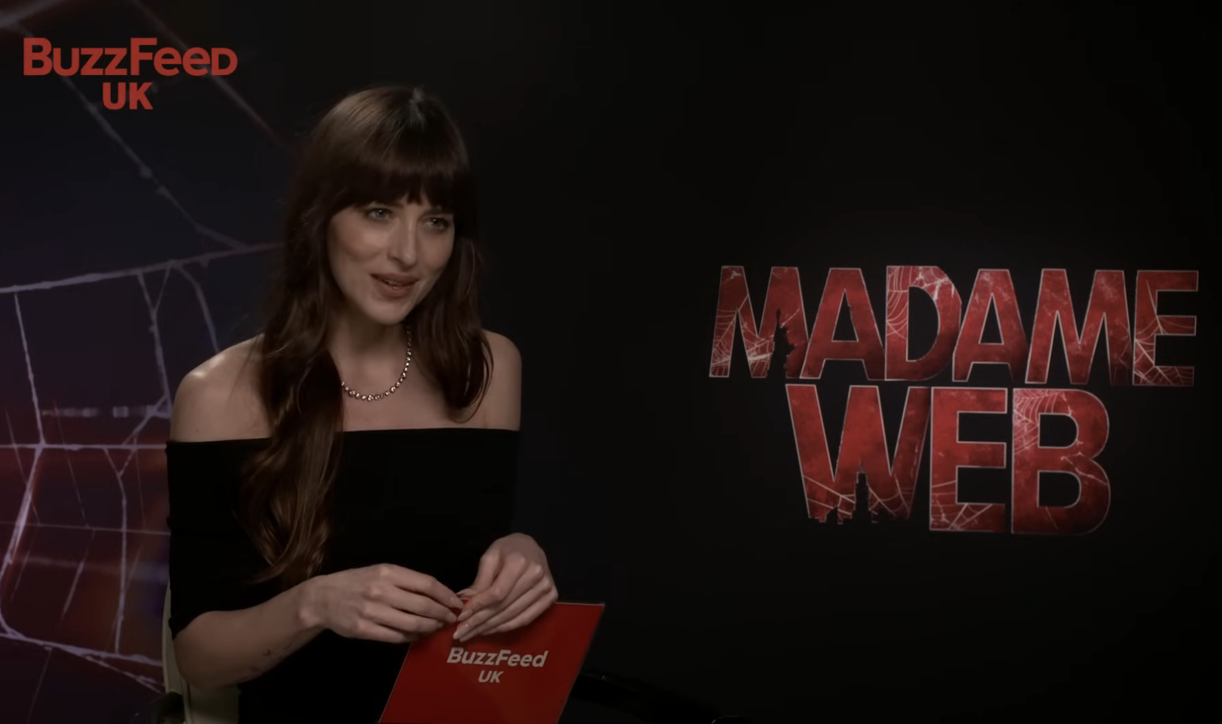 Dakota Johnson reads iconic movie lines while promoting Madame Web; dressed in black, seated with cards