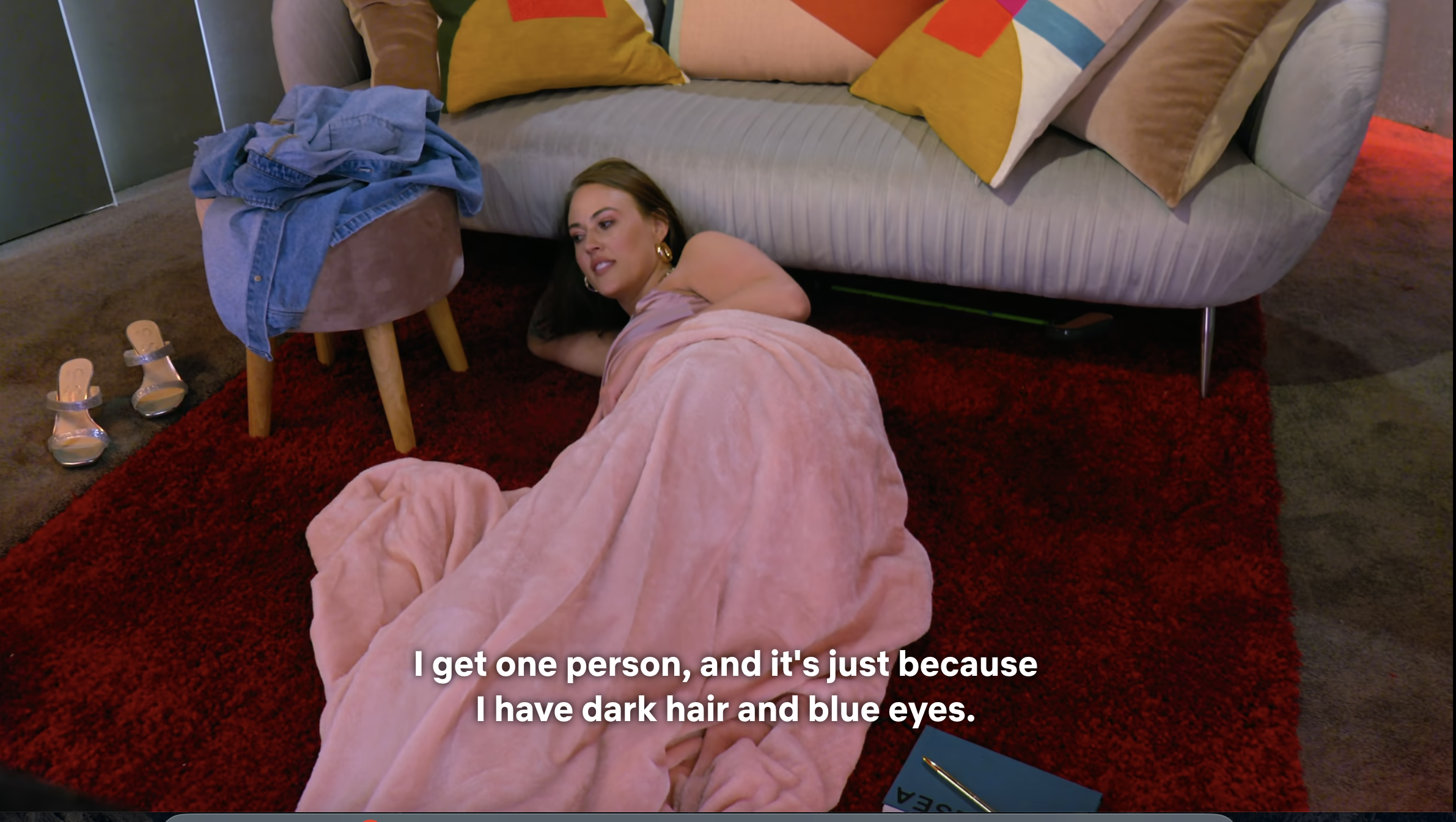 Person in a floor-length pink gown lying on a couch, speaking, with caption about having dark hair and blue eyes