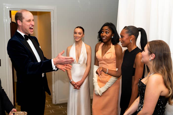 Prince William in a bow tie and suit greeting the four women at an event, who are all wearing elegant dresses