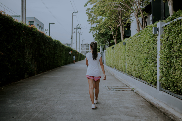 Person walking away on a paved path with greenery on sides