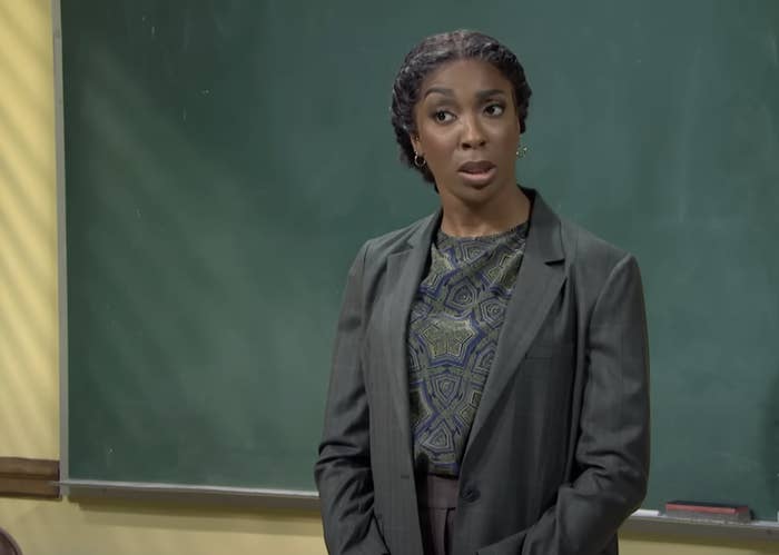 Woman in a blazer standing in front of a classroom chalkboard, looking surprised