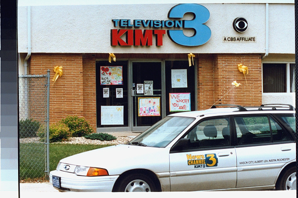 Television station KIMT building with a news vehicle parked in front. Posters in windows show support for a cause