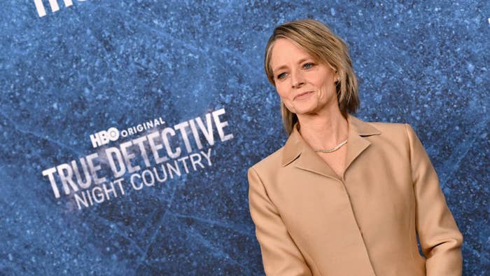 Jodie Foster standing in front of a backdrop with &quot;HBO Original True Detective Night Country&quot; text, wearing a stylish beige suit