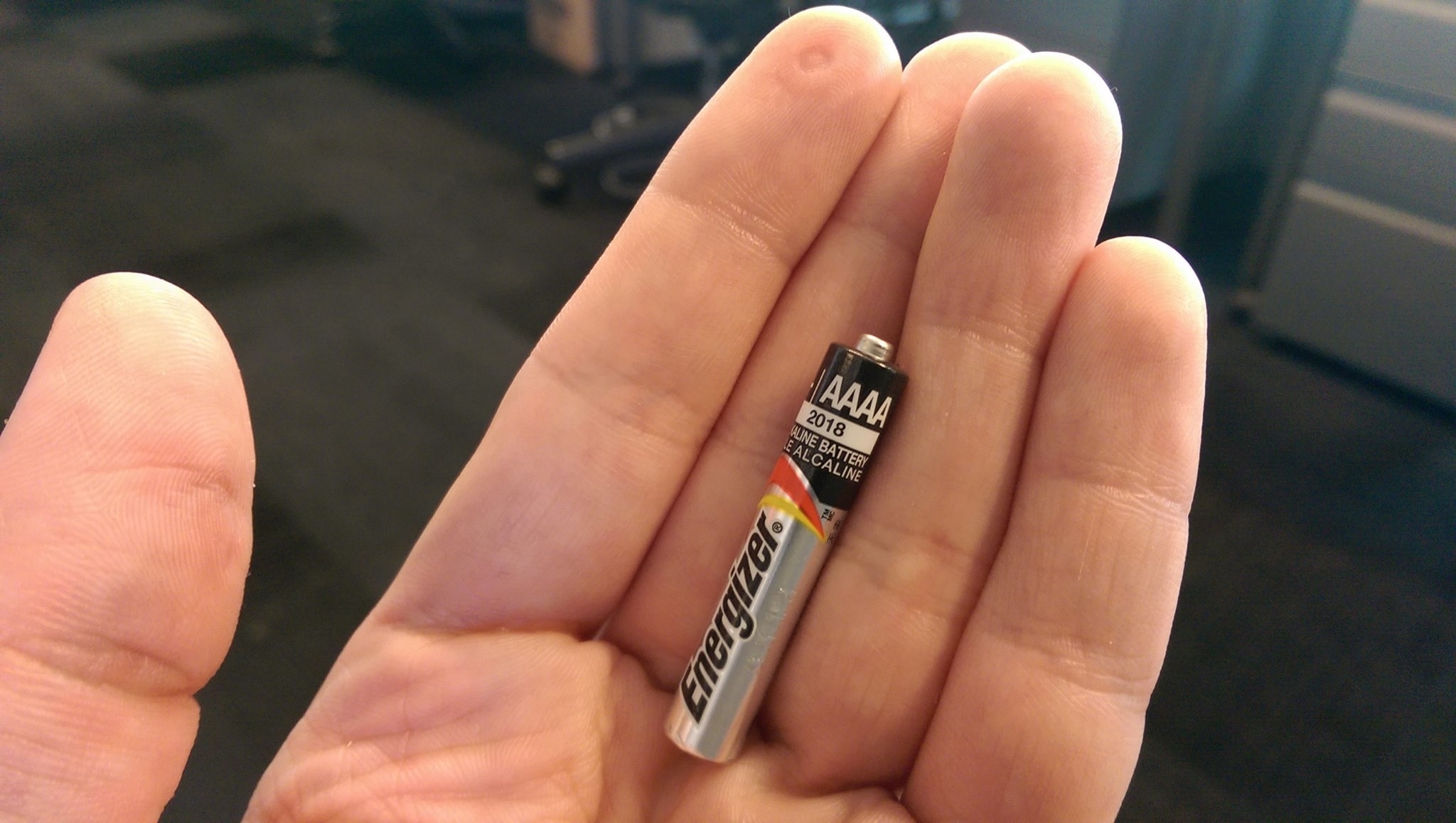 Person&#x27;s hand holding a small AAAA Energizer battery to show its size compared to fingers