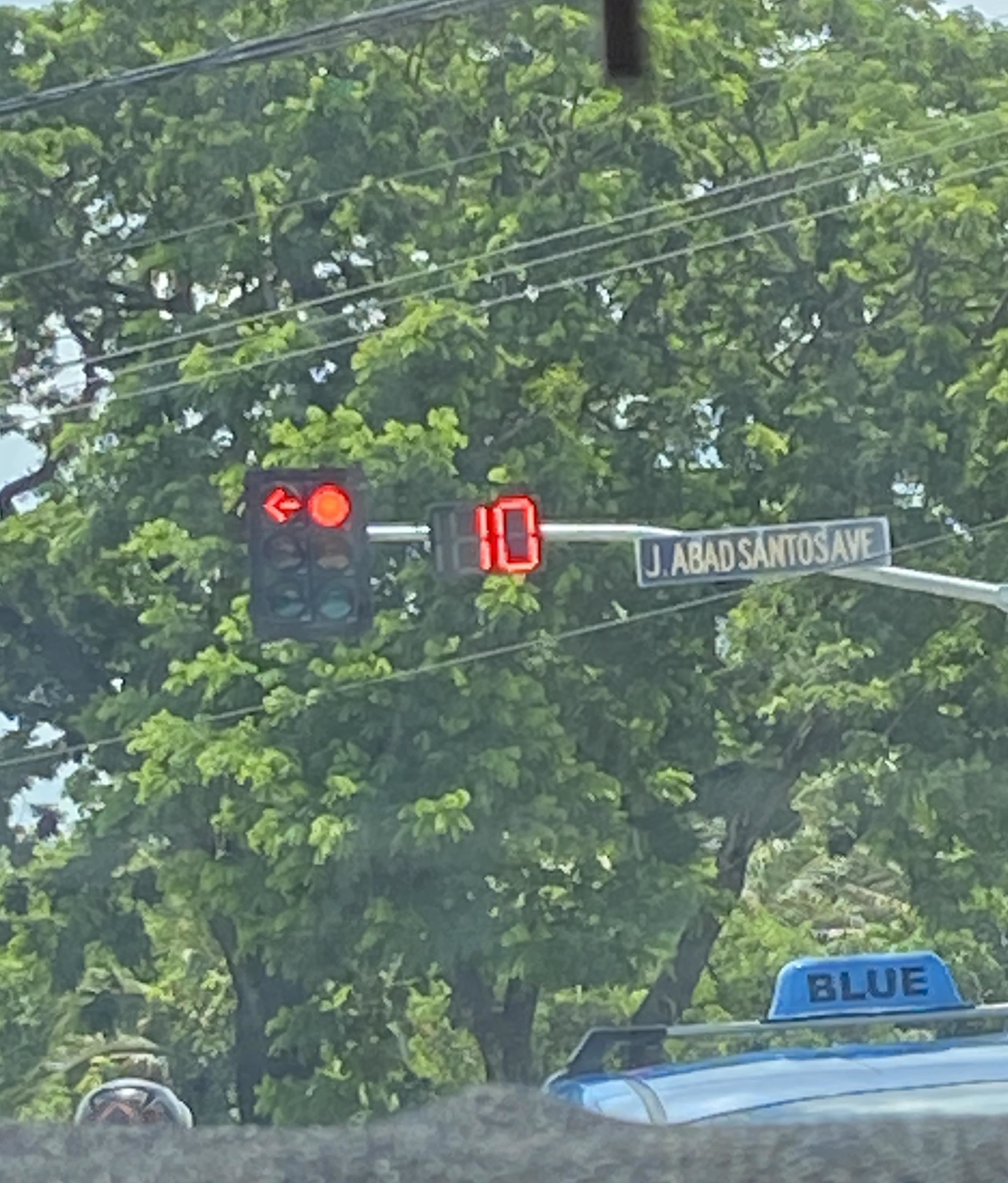 Red traffic light with a timer showing ten seconds at J. Abad Santos Avenue, framed by greenery
