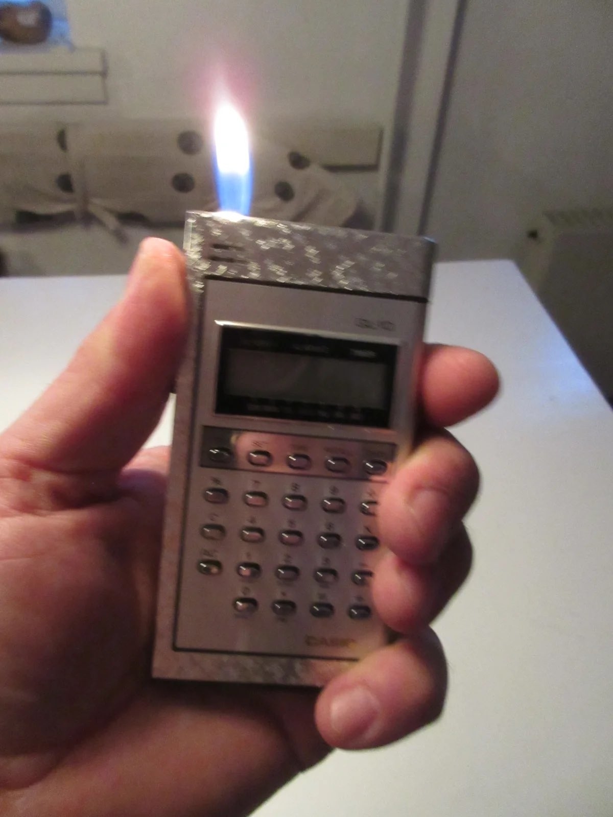 Person holds a vintage calculator with a lit lighter on top, juxtaposing old technology with traditional lighting