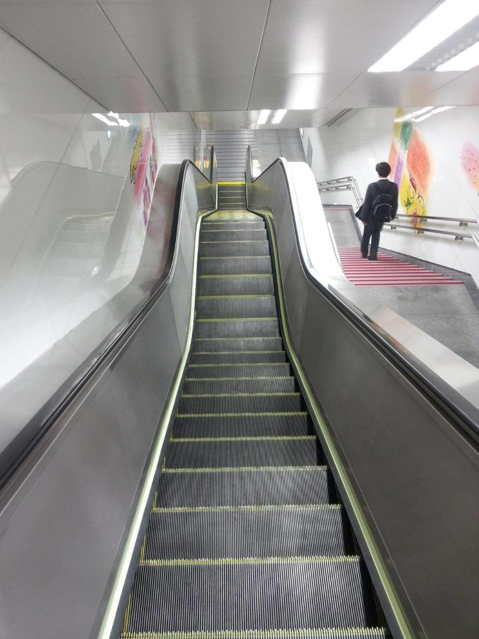 Escalator with yellow safety striping on steps; instead of a constant decline to the bottom, the escalator has a section in the middle that runs straight across