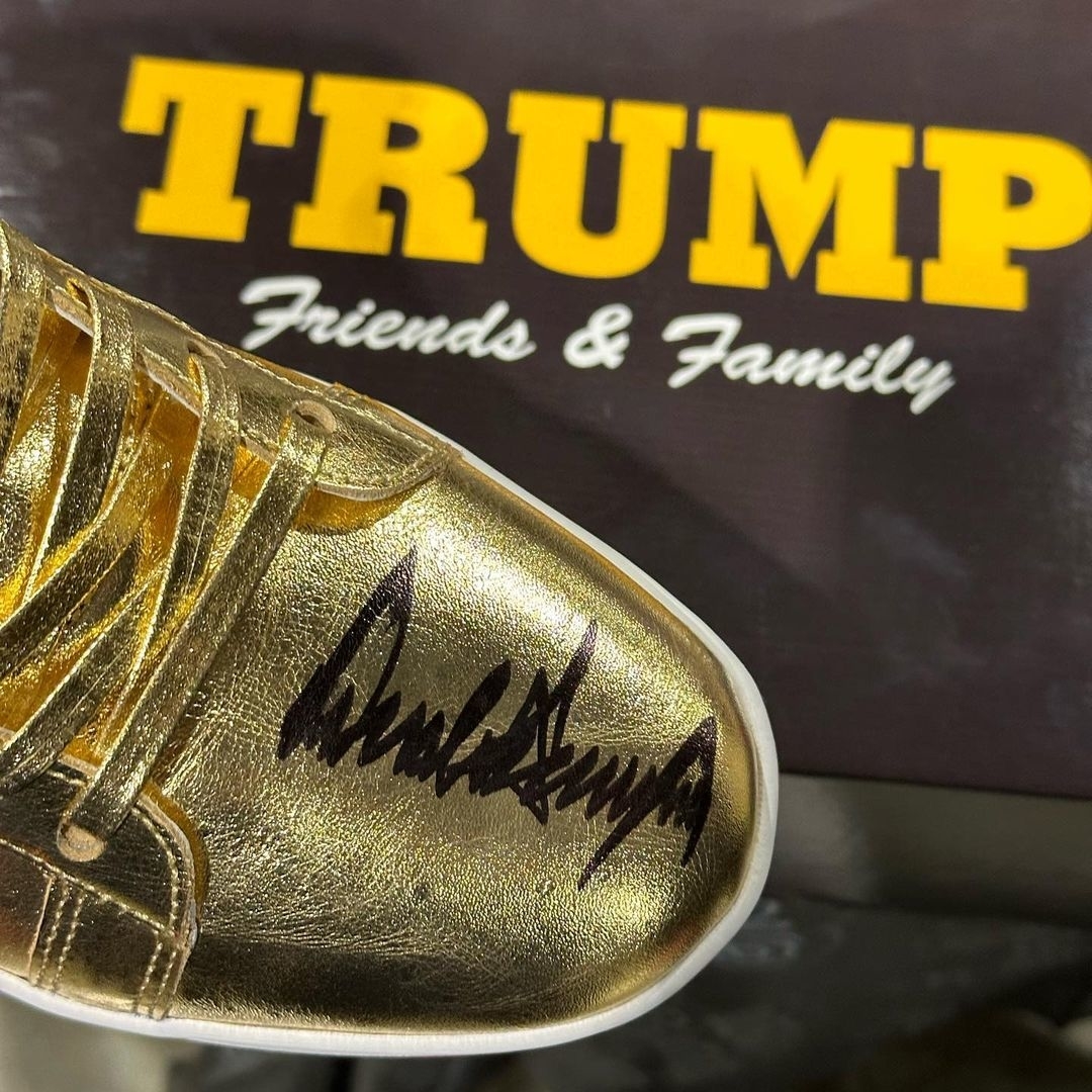 Gold sneaker with signature on the toe, in front of a sign reading &quot;TRUMP Friends &amp; Family&quot;