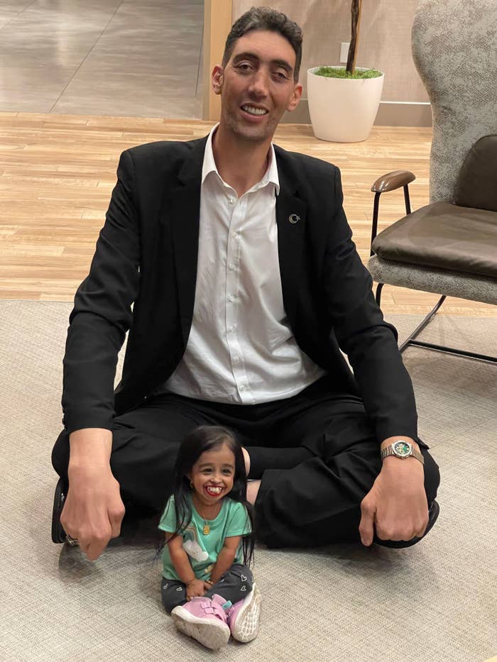 Man in a suit sitting next to a smiling small person indoors