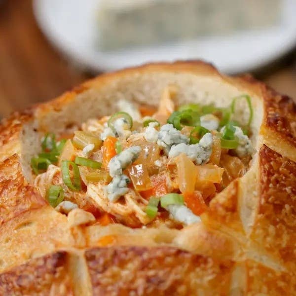 A bread bowl filled with chicken and topped with blue cheese and sliced green onions