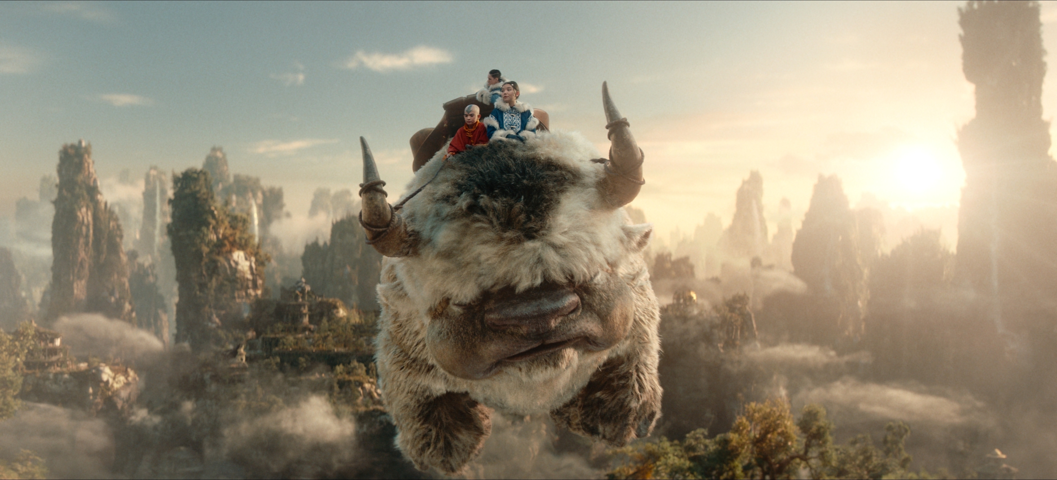 A group of animated characters riding on a flying bison above a forested landscape