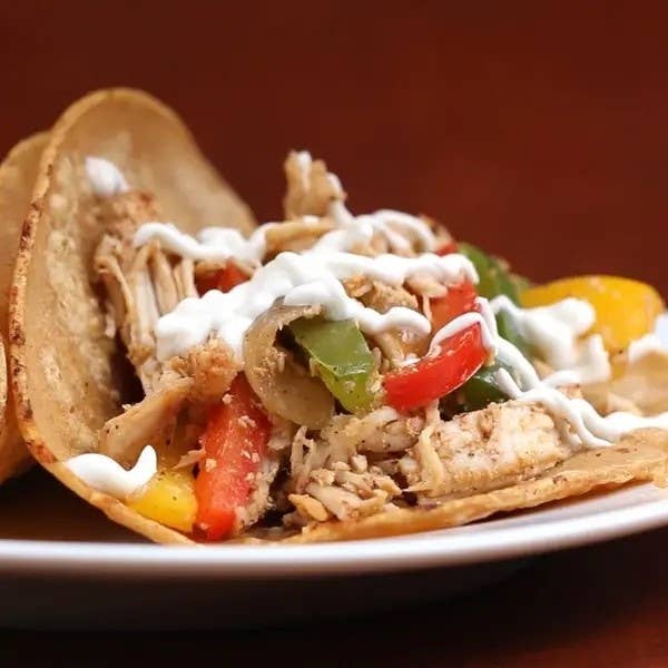 Chicken fajita in a tortilla with sautéed peppers, onions, and a drizzle of sour cream
