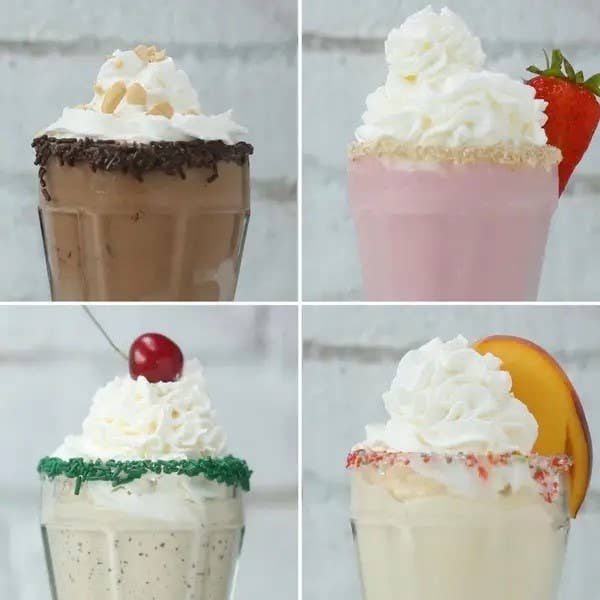 Four assorted milkshakes topped with whipped cream and garnishes like fruit and sprinkles