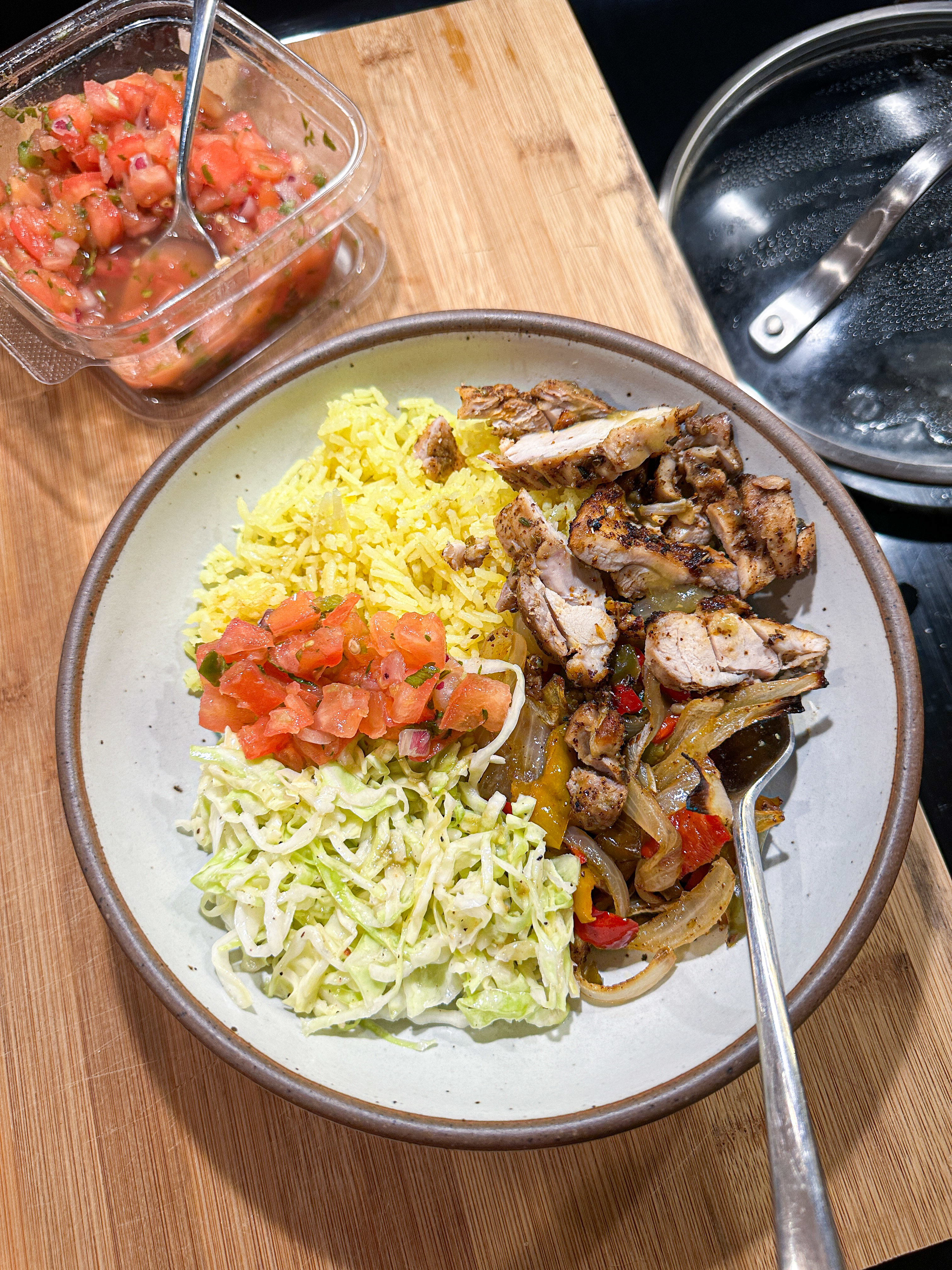 A plate of food with rice, grilled chicken, sautéed vegetables, shredded lettuce, and diced tomatoes next to a container of salsa