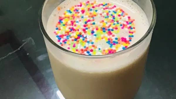 A glass of milkshake topped with multicolored sprinkles