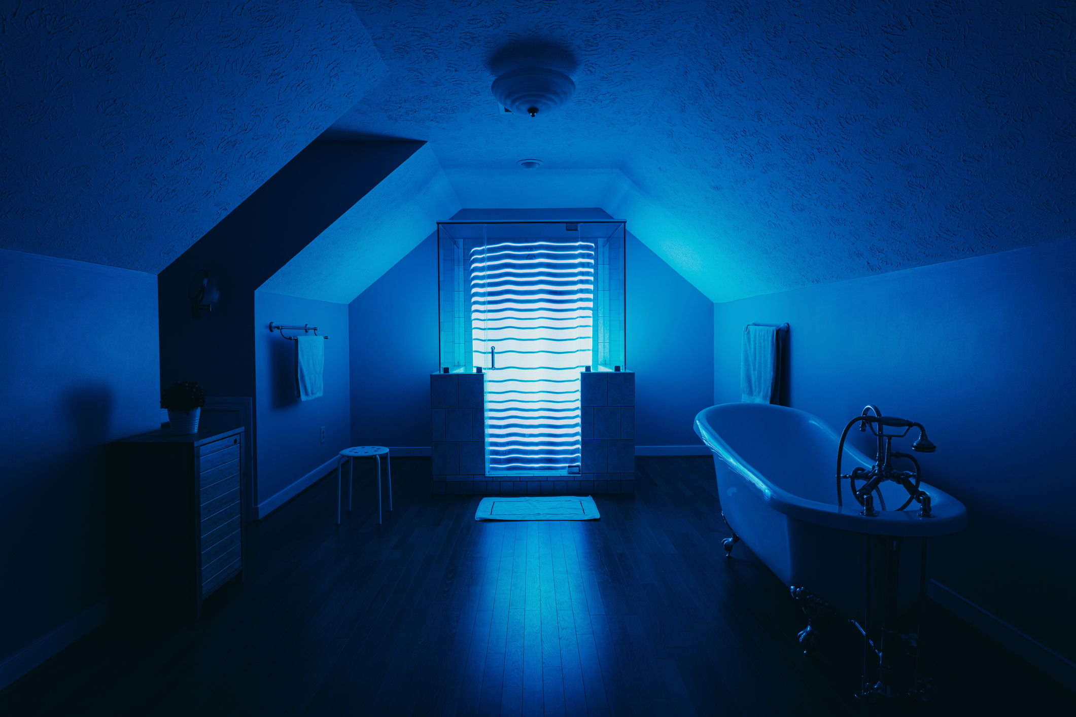 A dimly lit attic bathroom with a freestanding tub and an illuminated patterned window