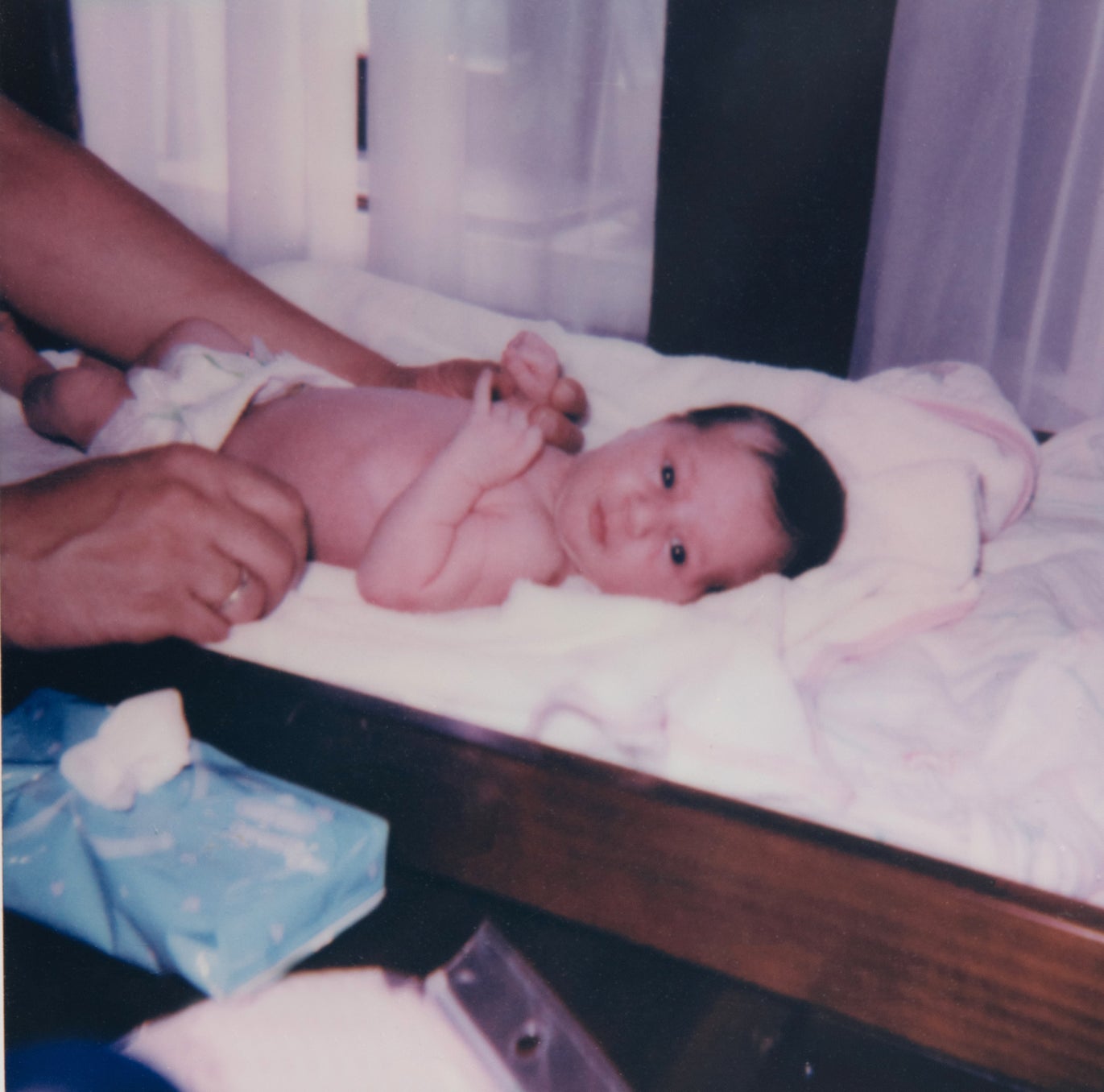 Infant lying on a changing table with an adult&#x27;s hands gently securing the baby
