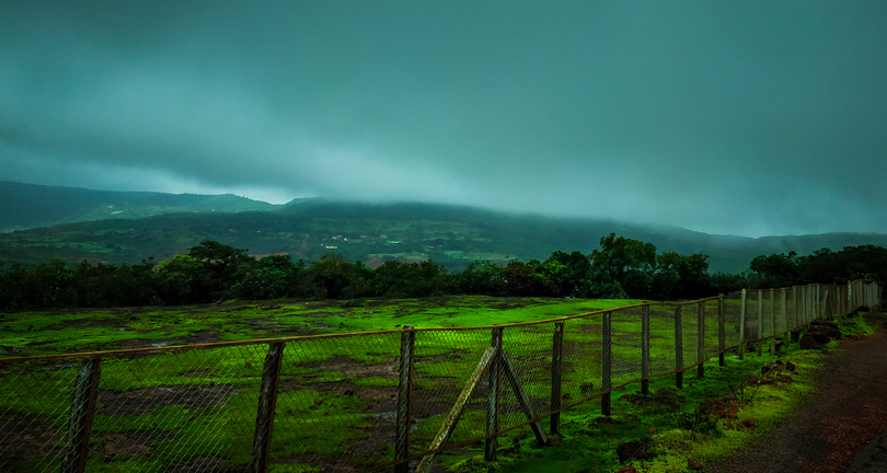 Misty landscape with grass field, fence, and hills in the background