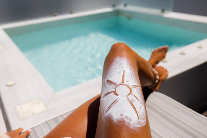 Person applying sunscreen on leg by a pool, showcasing sun protection importance for shoppers