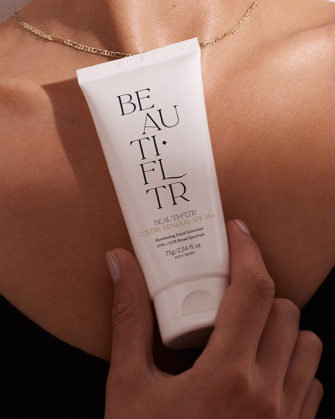 Close-up of hands holding a tube of BEAUTIFLTR sunscreen against bare skin