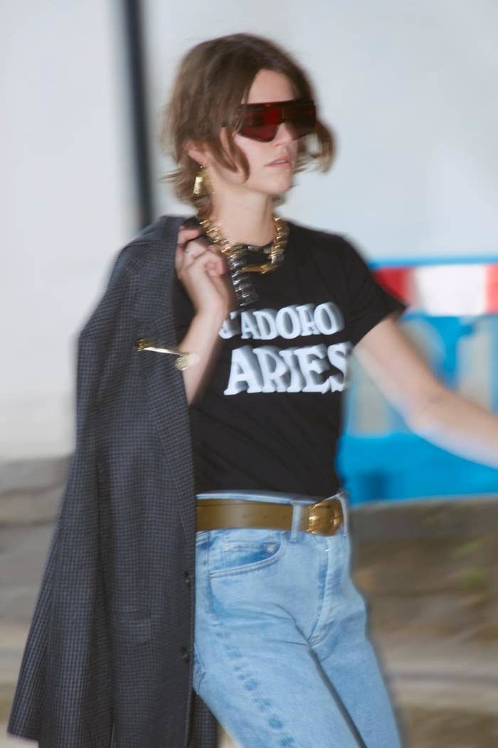 Woman in graphic tee, oversized blazer, jeans, and sunglasses walking