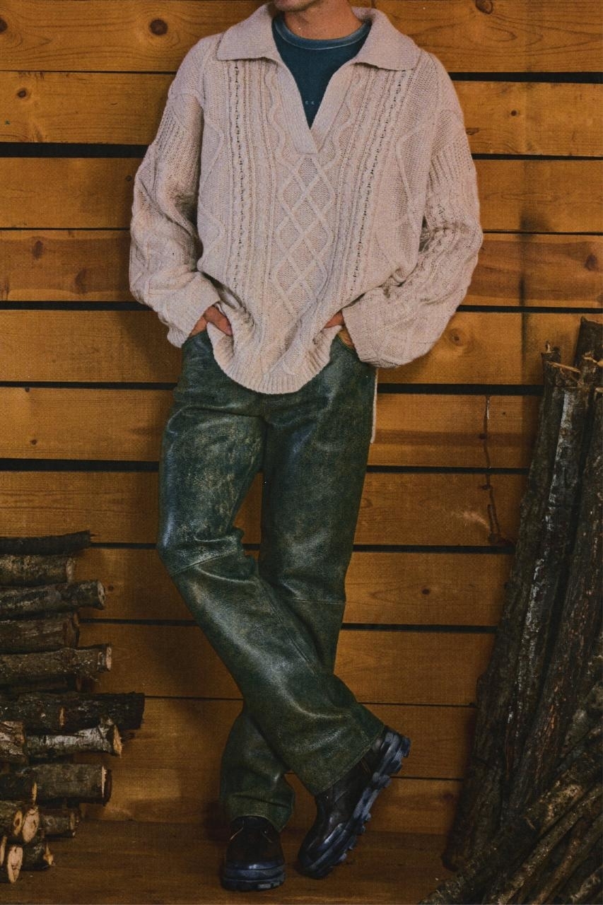 Person in oversized cable-knit sweater, wide-leg jeans, and chunky shoes, standing with hands in pockets