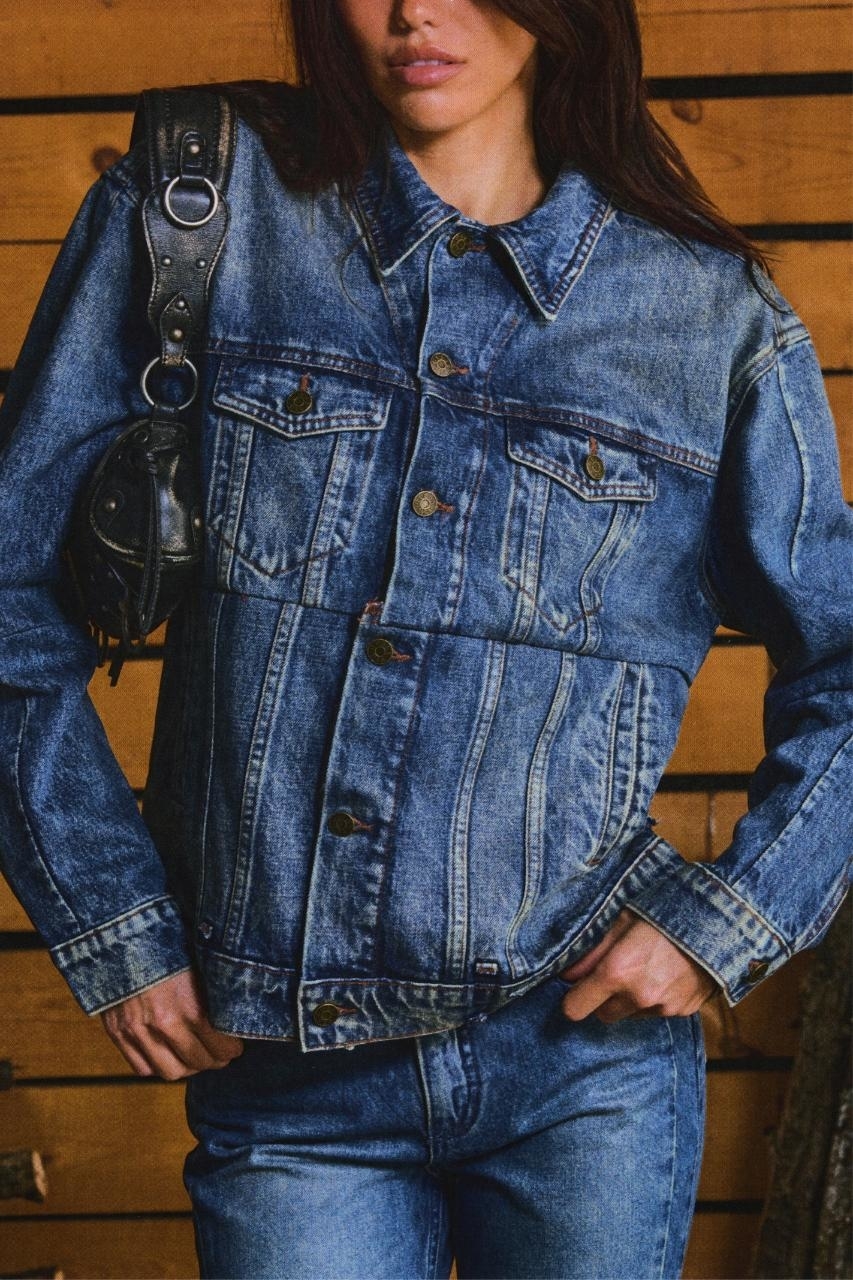 A person in a denim jacket and jeans with a small shoulder bag