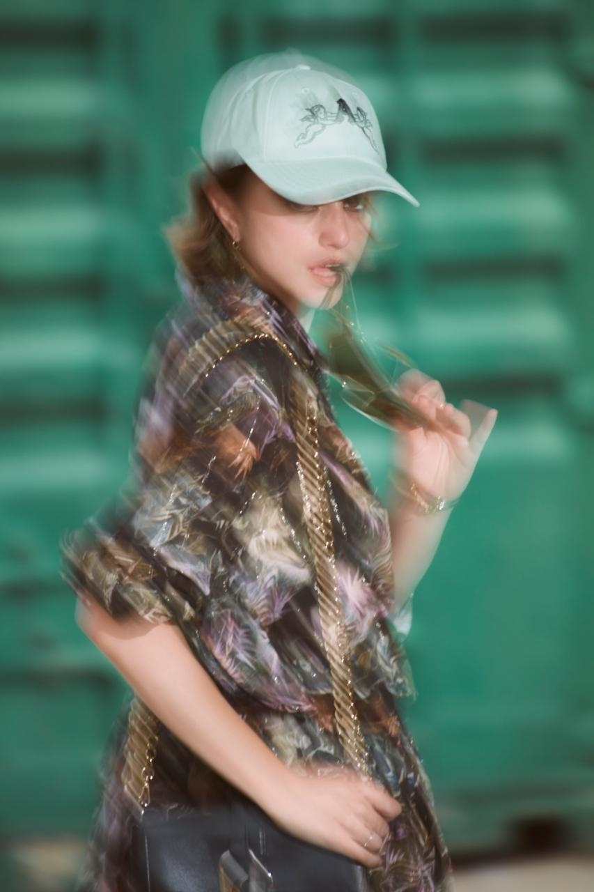 Person in a cap and patterned top with chains poses with motion blur