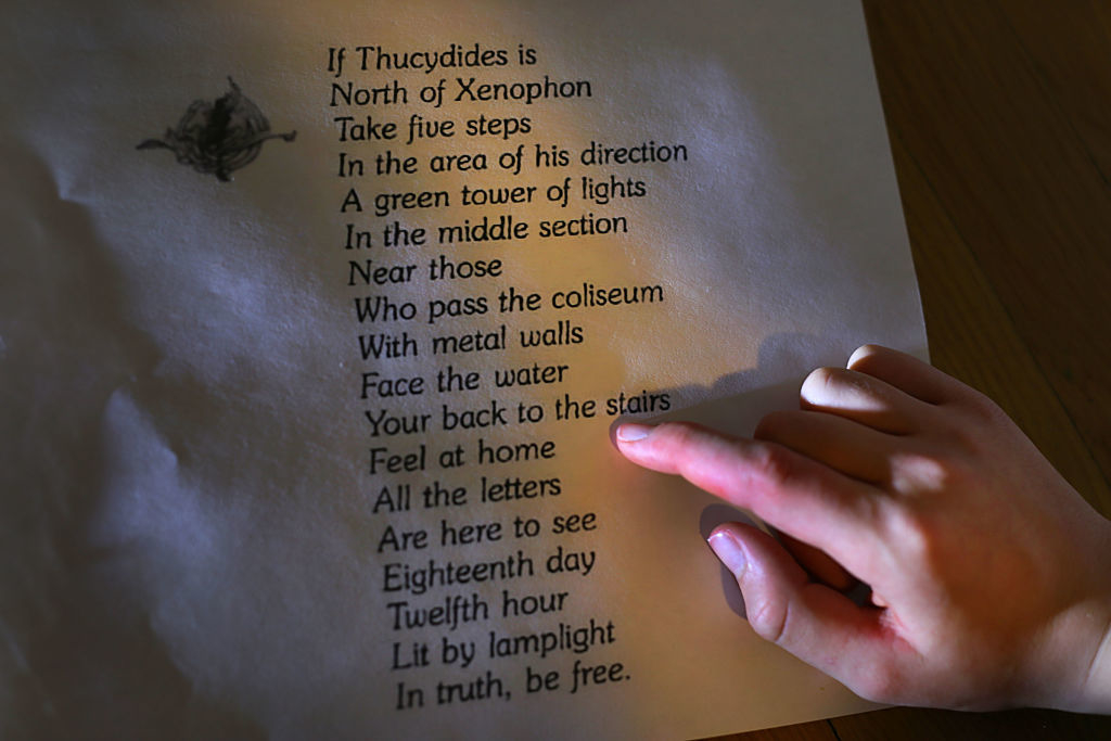 Person&#x27;s hand pointing to a poem on paper with shadowy light, text partially readable, about ancient wisdom and direction