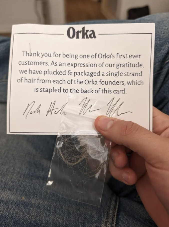 Hand holding a thank-you card and a bag with a single strand of hair from the Orka founders