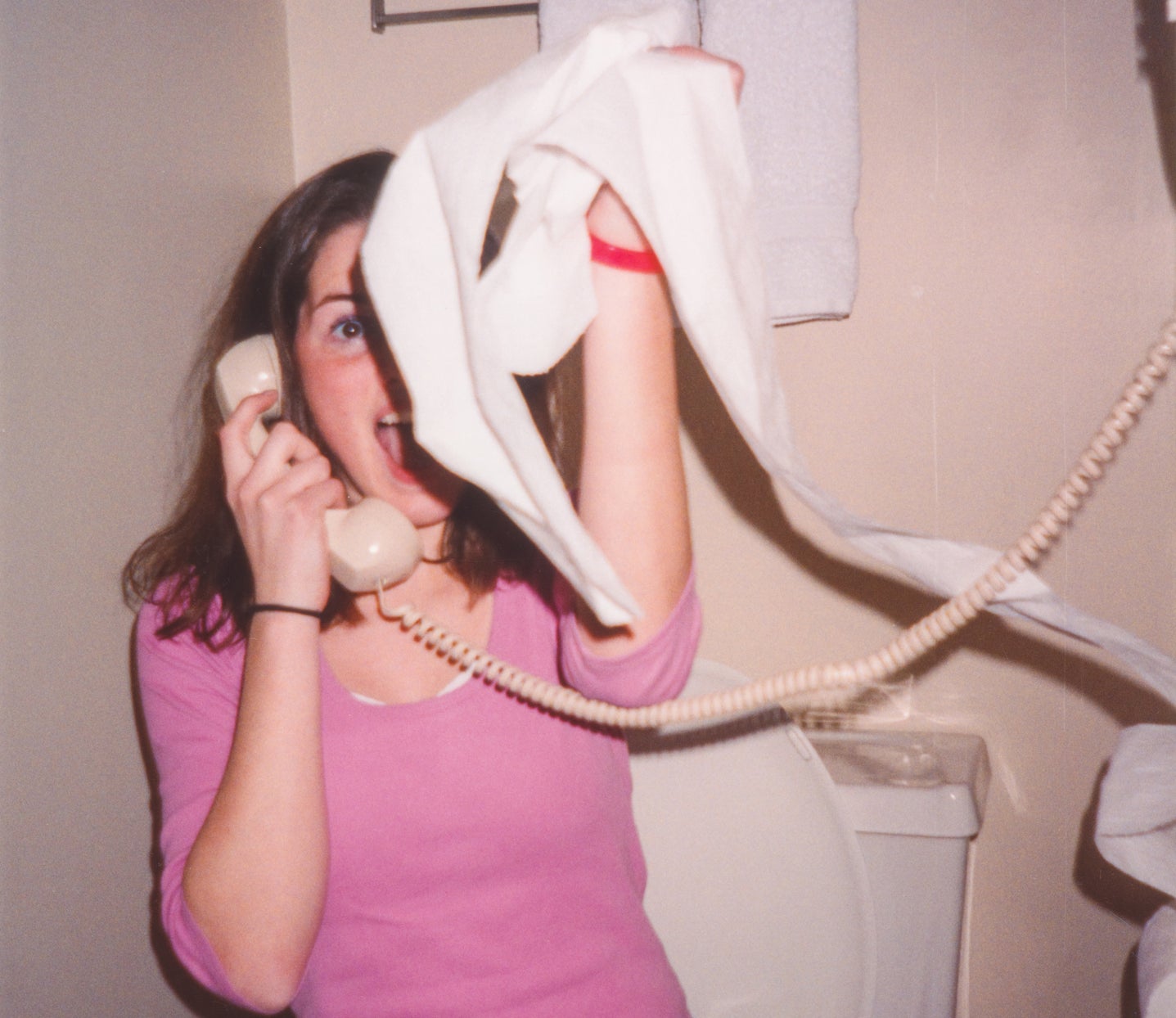 Woman on a corded phone making a face, caught off guard, with a towel in her hand, standing in a bathroom