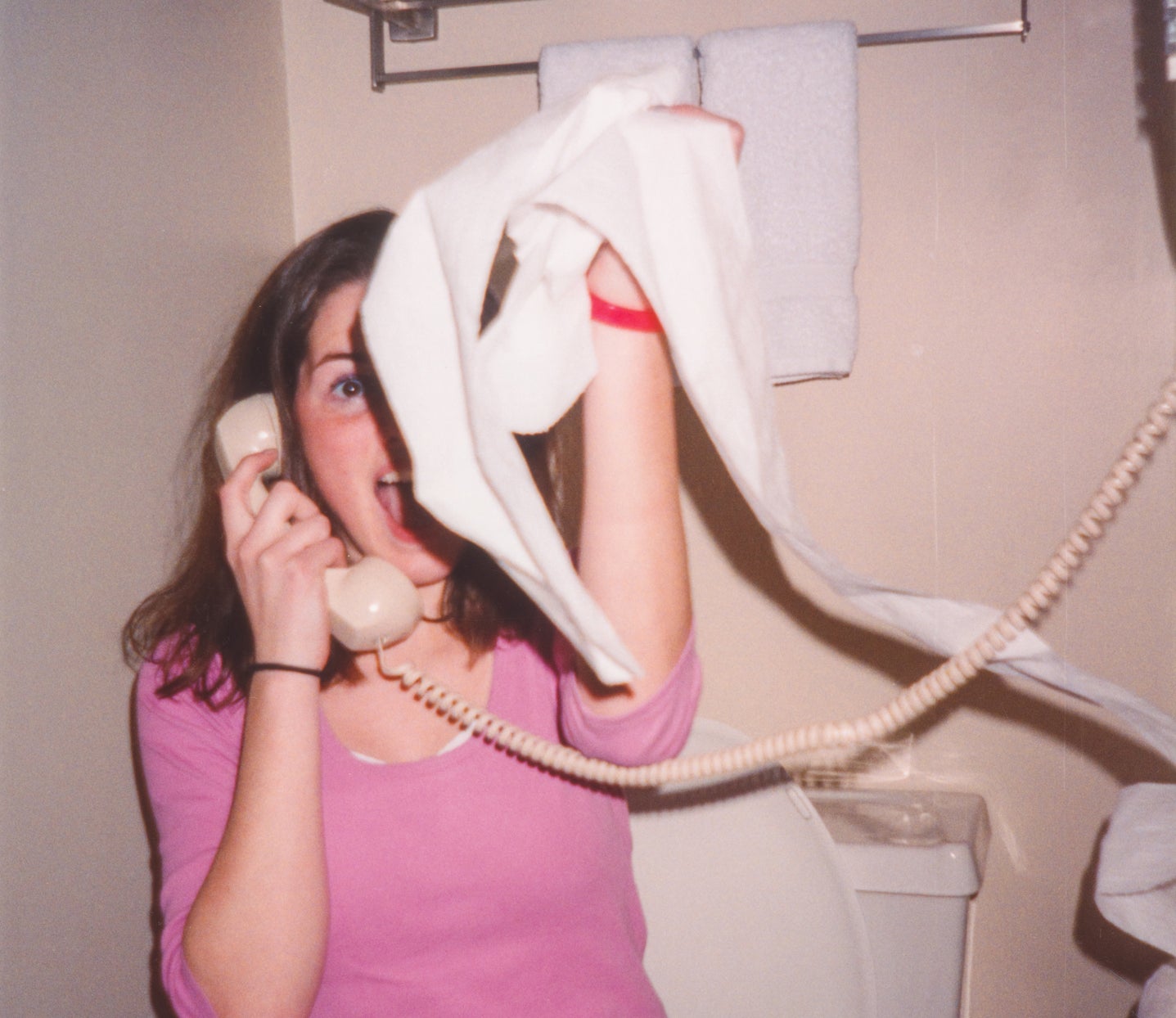 Woman on a corded phone making a face, caught off guard, with a towel in her hand, standing in a bathroom