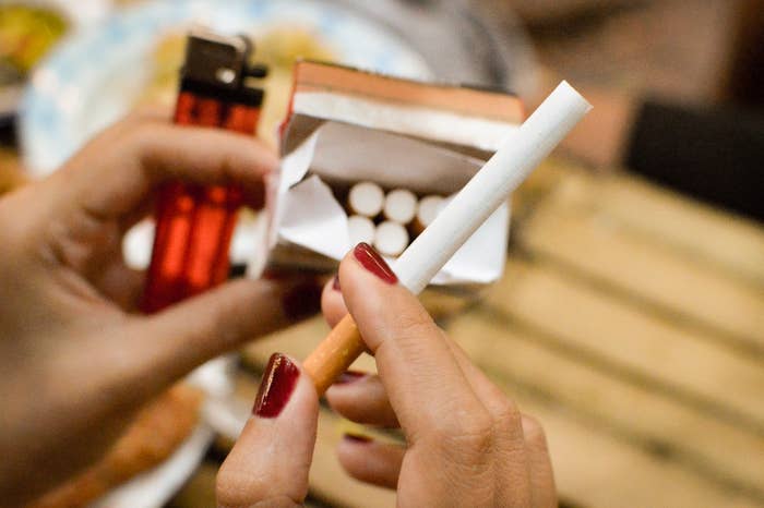 Person&#x27;s hand with red nails holding a cigarette and a box of matches