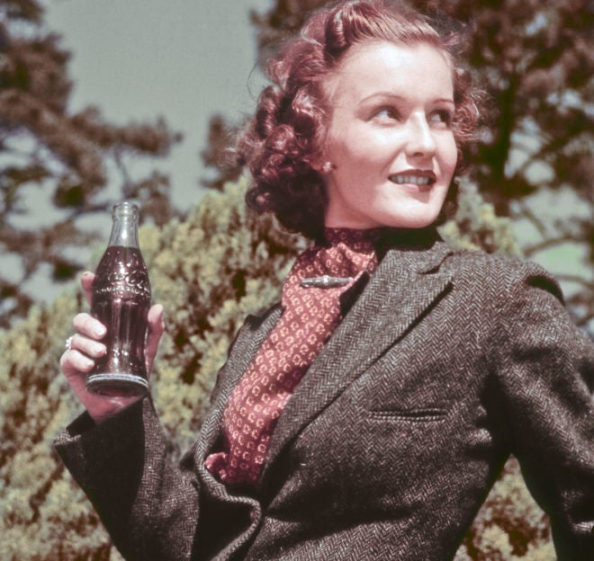 Woman from the past holding a Coca-Cola bottle, wearing a vintage suit, with a natural backdrop