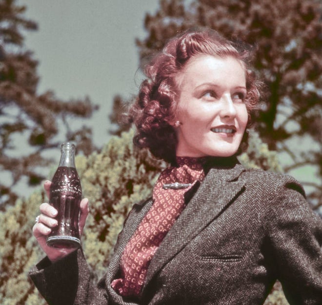 Woman from the past holding a Coca-Cola bottle, wearing a vintage suit, with a natural backdrop