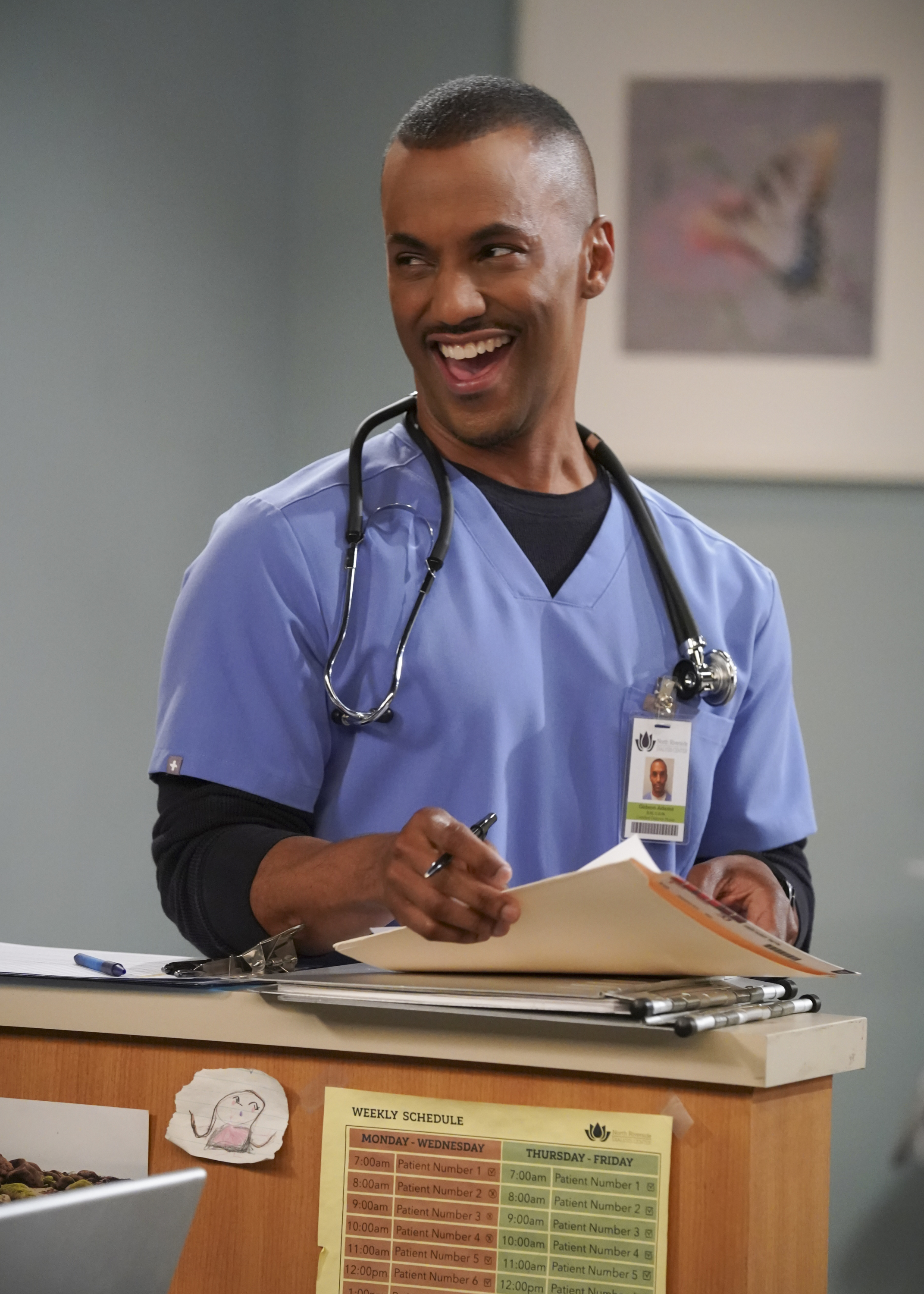 Darryl in character wearing a medical scrub with a stethoscope, smiling while reading a paper