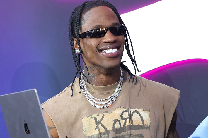 Travis Scott in a graphic tee smiles at a music event