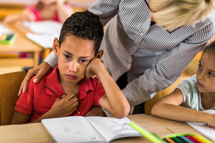 Teacher comforting a distressed boy in a classroom while other children continue working